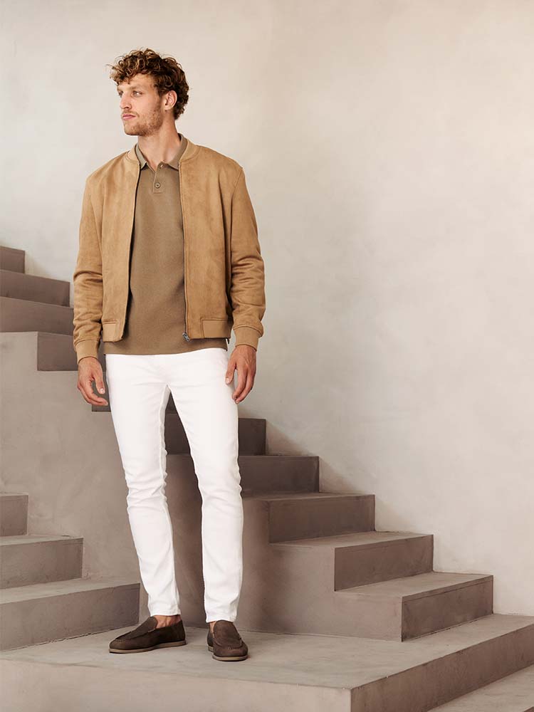 Man in witte Bukser jeans met beige polo en jas