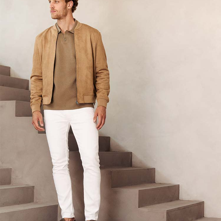 Man in witte Bukser jeans met beige polo en jas