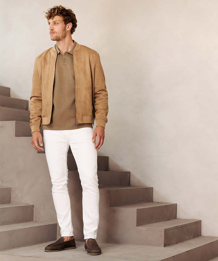 Man in witte Bukser jeans met beige polo en jas