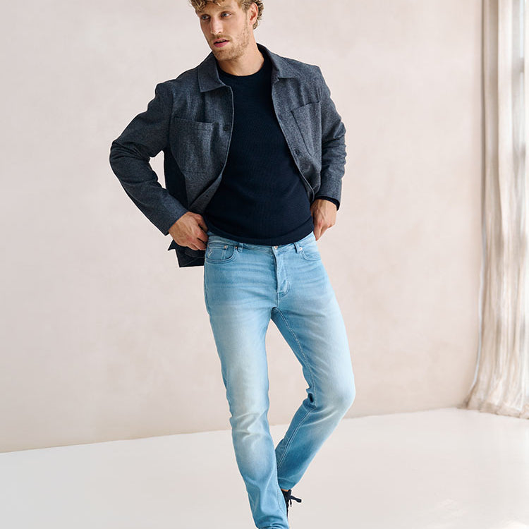 Man in lichtblauwe Bukser jeans en donkerblauwe trui en grijze jas