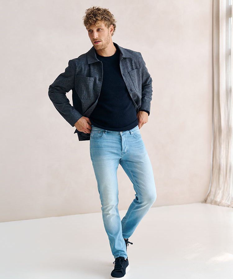 Man in lichtblauwe Bukser jeans en donkerblauwe trui en grijze jas