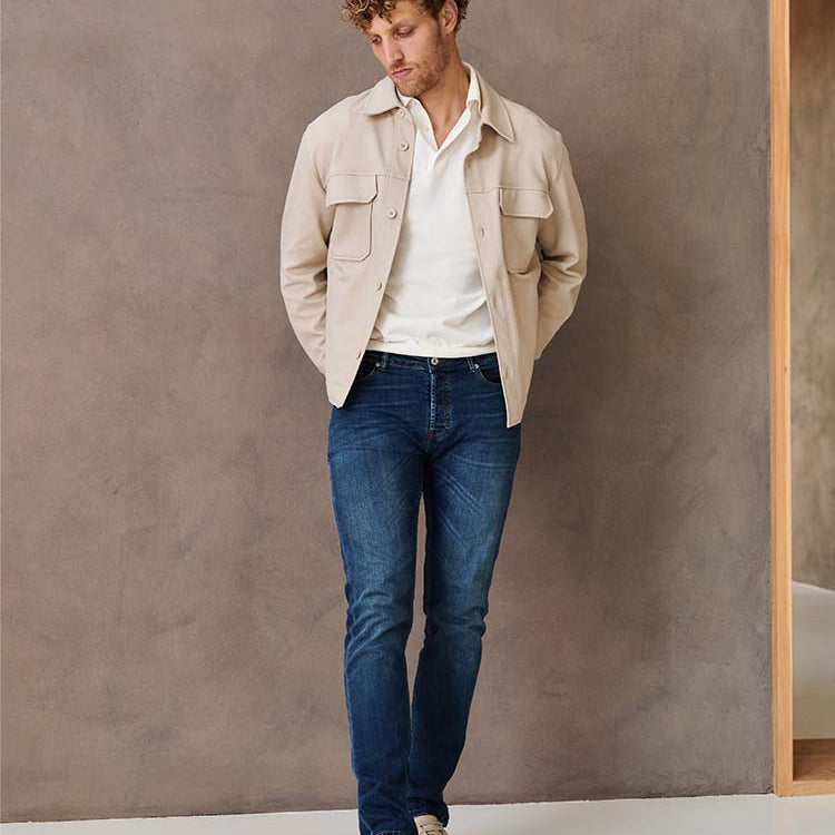 Man in donkerblauwe Bukser jeans, witte polo en beige jas