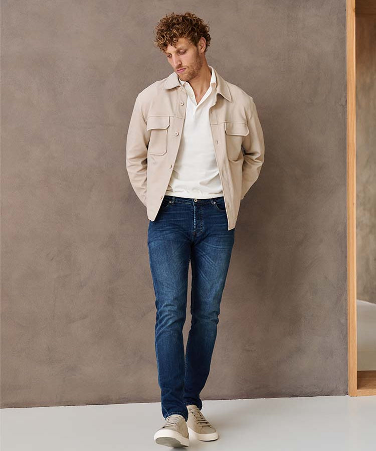Man in donkerblauwe Bukser jeans, witte polo en beige jas