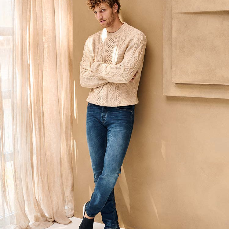 Man in blauwe Bukser jeans en beige wollen trui