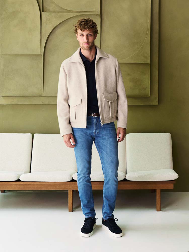 Man in lichtblauwe Bukser jeans met beige jasje en donkerblauwe polo