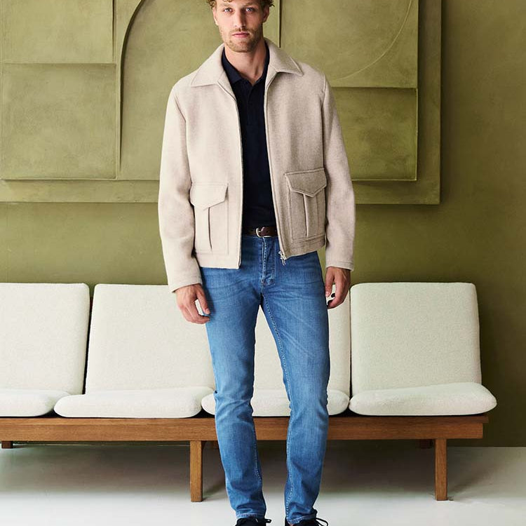 Man in lichtblauwe Bukser jeans met beige jasje en donkerblauwe polo
