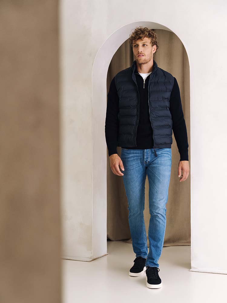 Man in ichtblauwe Bukser jeans, zip trui en bodywarmer