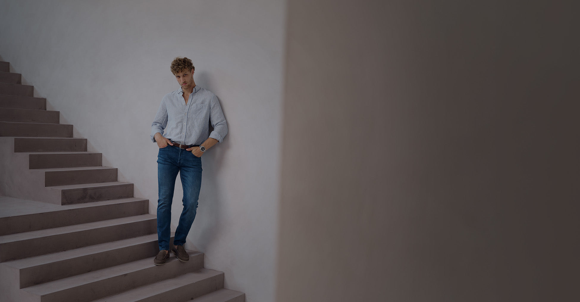Man in gestreept overhemd en donkerblauwe jeans op een trap